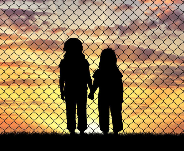two children behind chain-link fence holding hands