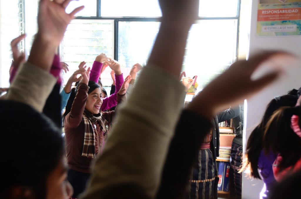 Starfish impact school photo taken through raised hands at forefront, students excited about learning. Starfish was CIG recipient in 2015.