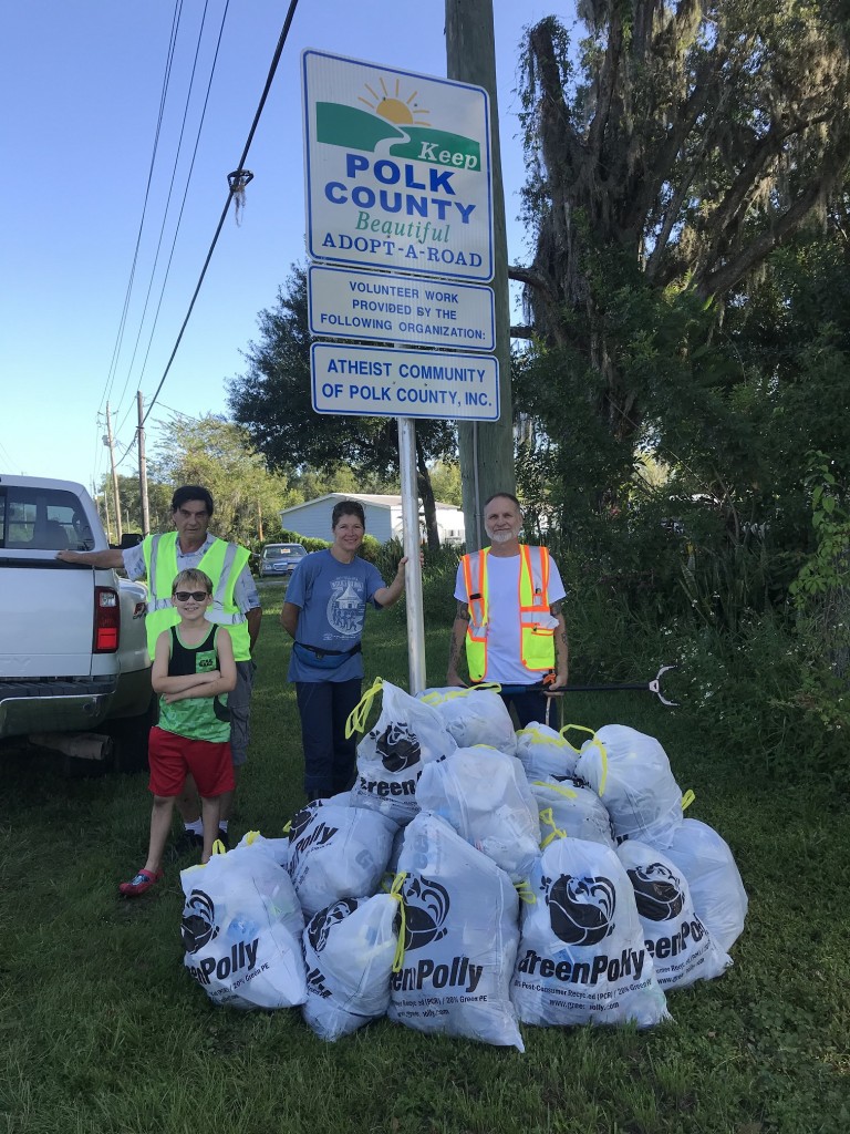 Atheist Community of Polk County pose with a pile of full trash bags in front of their Adopt-A-Road sign